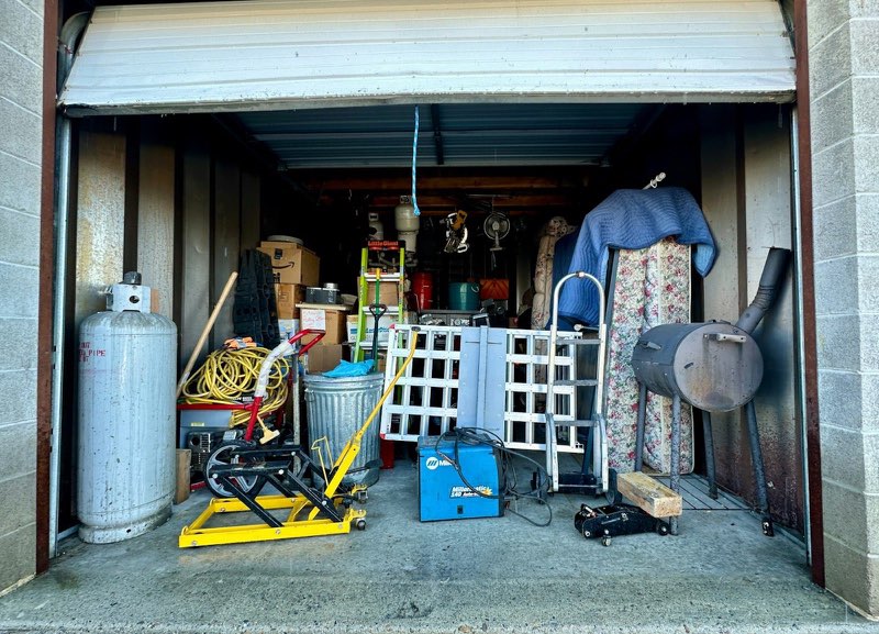 A storage unit packed to the roof with a mattress, ladders, a welder, a propane tank and stacked boxes — a typical cleanout before we start.