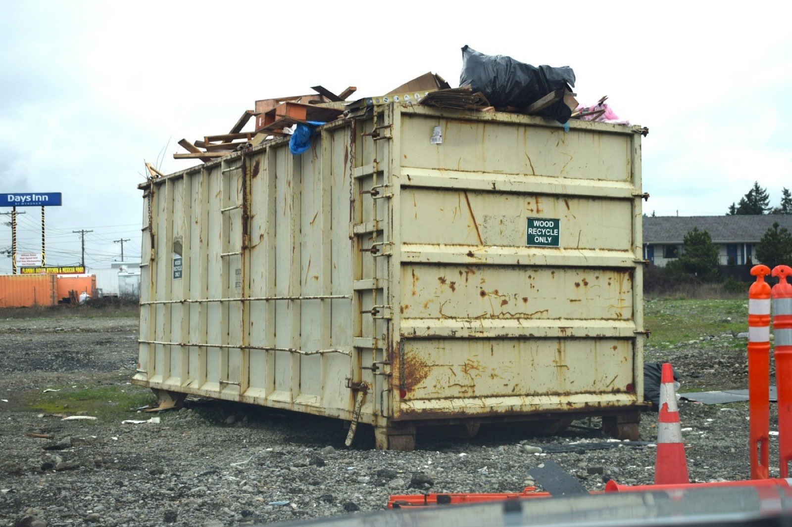 A roll-off container marked WOOD RECYCLE ONLY, loaded with timber and bagged waste.
