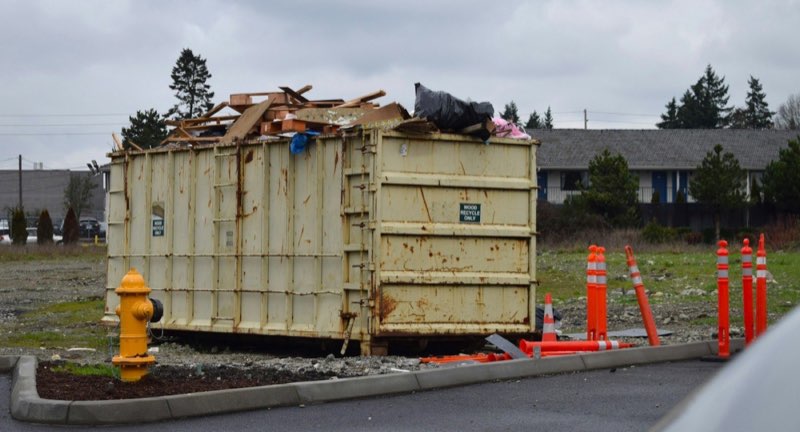 A roll-off container on a cleared lot, filled with construction timber and debris.