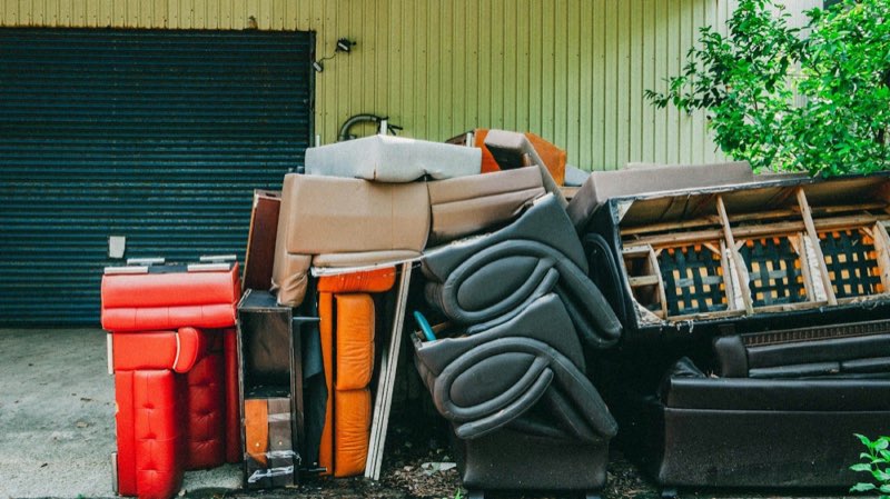 Sofas, armchairs and a mattress stacked against a wall, ready to be taken away.